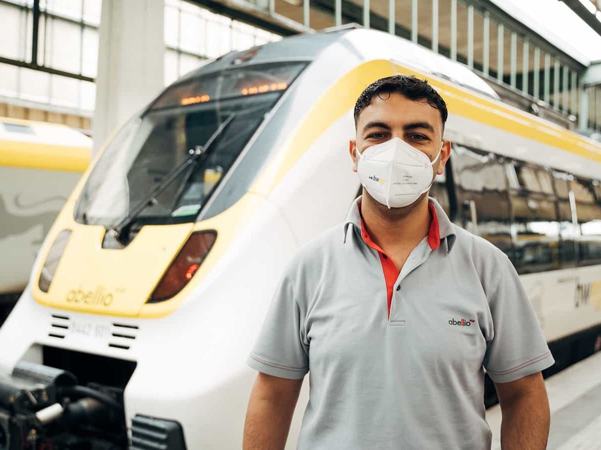 Lokführer mit Migrationshintergrund steht vor einer Bahn von bwegt.