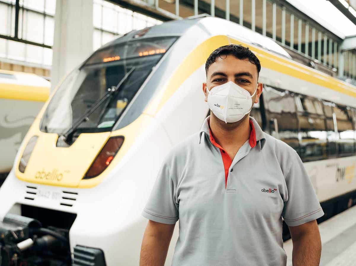 Lokführer mit Migrationshintergrund steht vor einer Bahn.