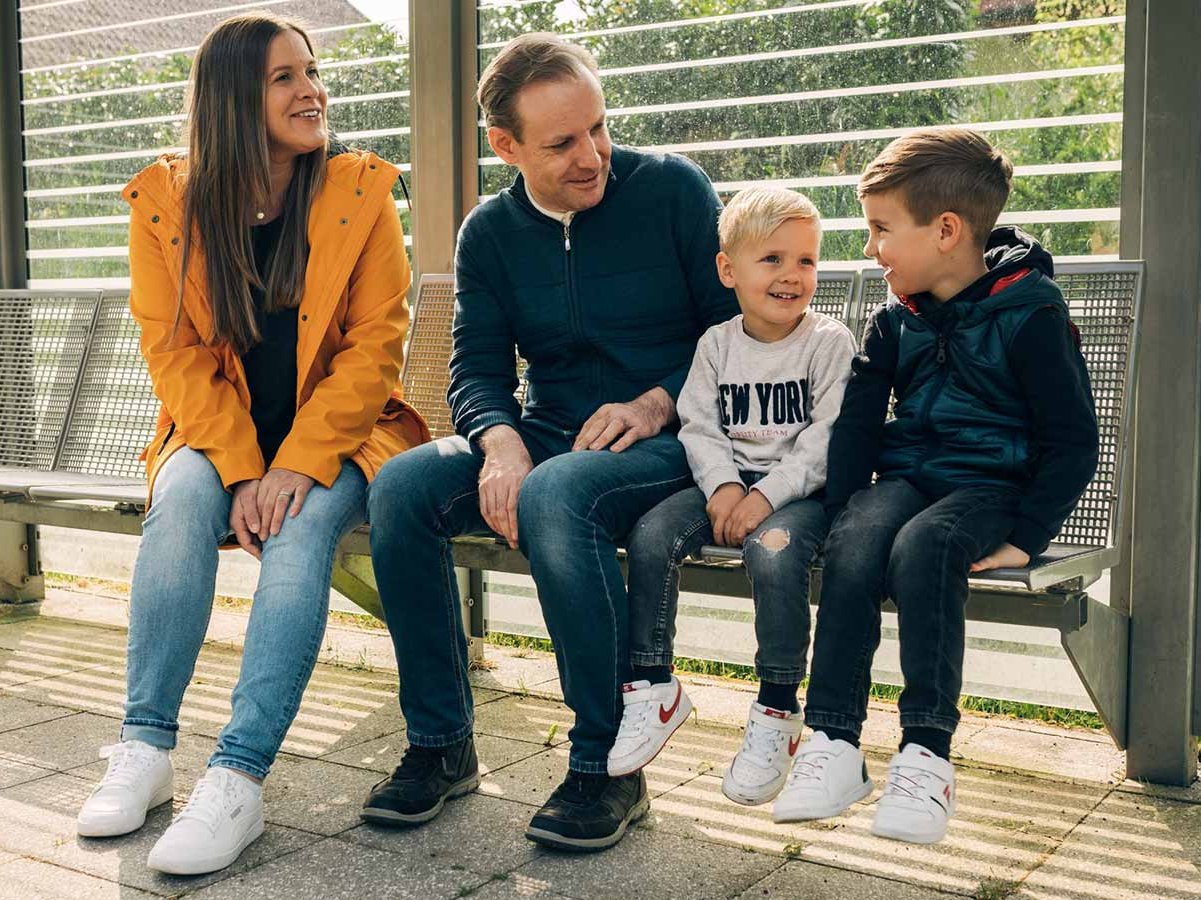 Familie mit zwei Kindern sitzt am Bahngsteig auf einer Bank.