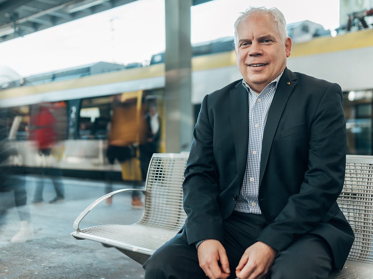 Mann im Anzug sitzt auf einer Bank am Bahnhof.