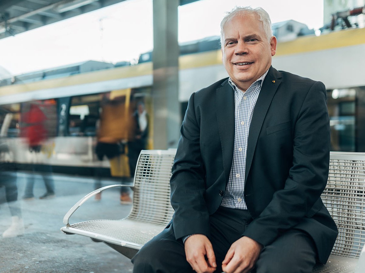 Mann im Anzug sitzt auf einer Bank im Bahnhof.