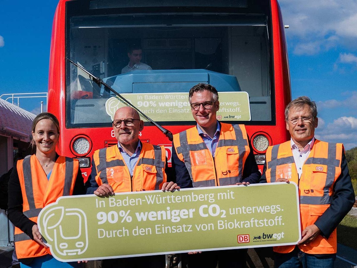 Vier Funktionäre des Verkehrsministeriums oder der Bahn stehen in Warnwesten vor einer Bahn.