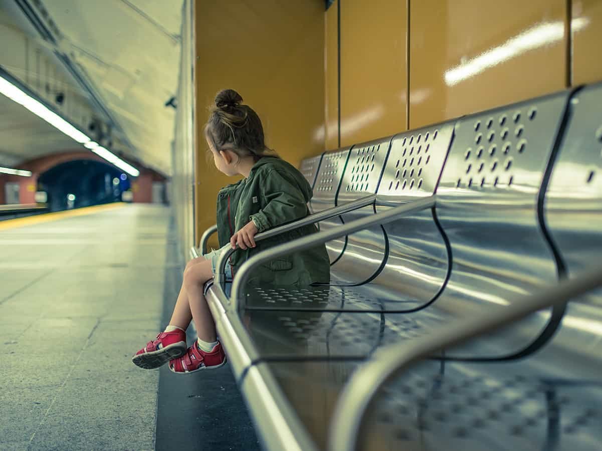 Kleines Mädchen sitzt alleine auf einer Bank am Bahnhof.