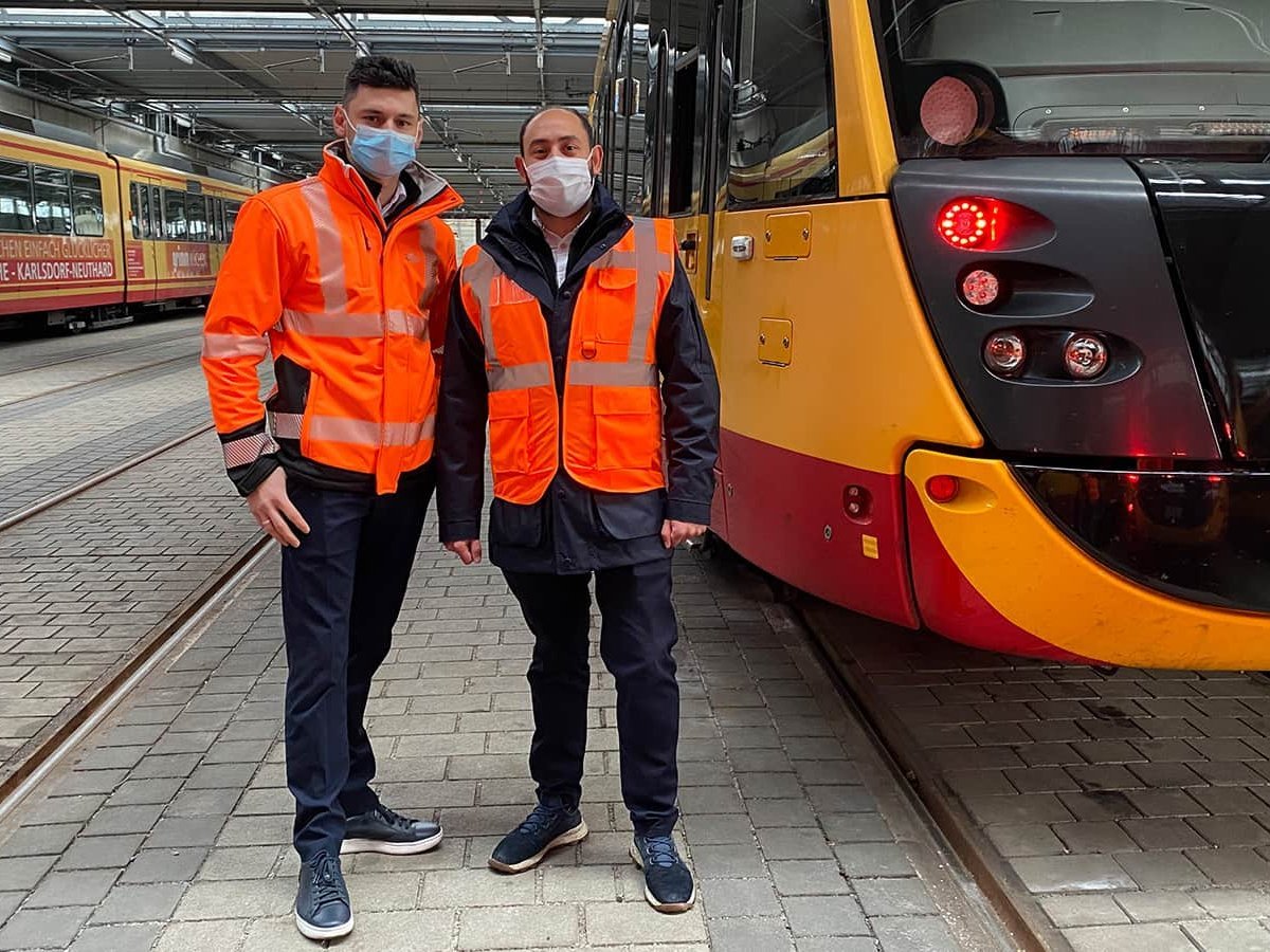 Zwei Lokführer mit Migrationshintergrund stehen vor einer Straßenbahn.