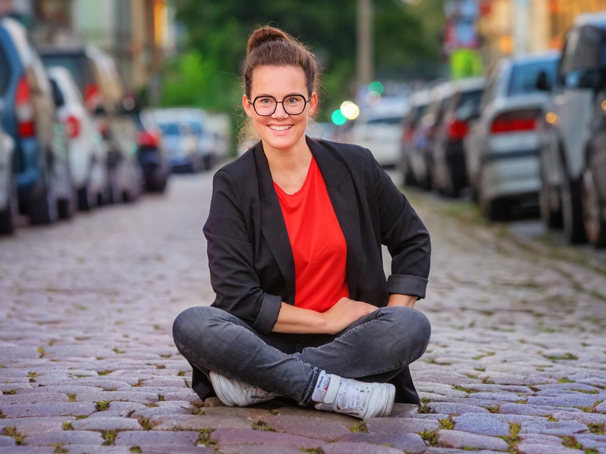 Frau sitzt auf einer Straße zwischen Autos im Schneidersitz.