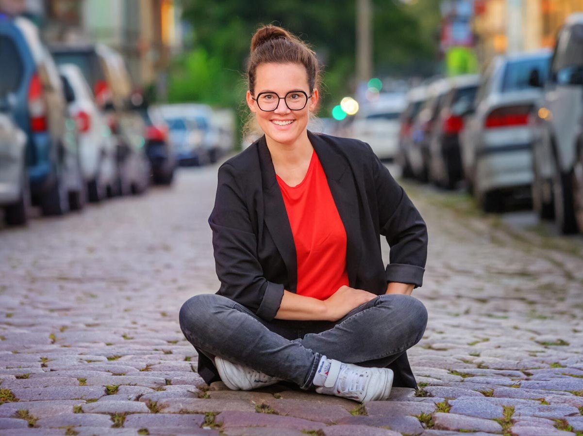 Frau sitzt im Schneidersitz auf der Straße zwischen Autos.