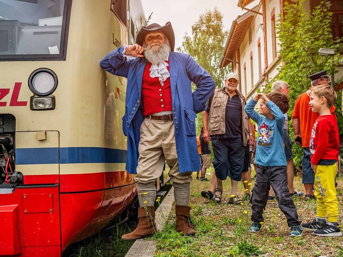 Mann in Räuber-Kostüm lehnt an einem Zug. Um ihn herum stehen Kinder.