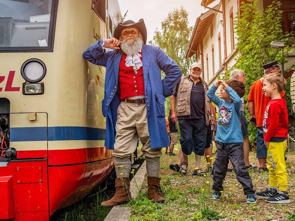 Ein als Räuber verkleideter Mann lehnt sich an einen Zug und Kinder stehen neben ihm. 