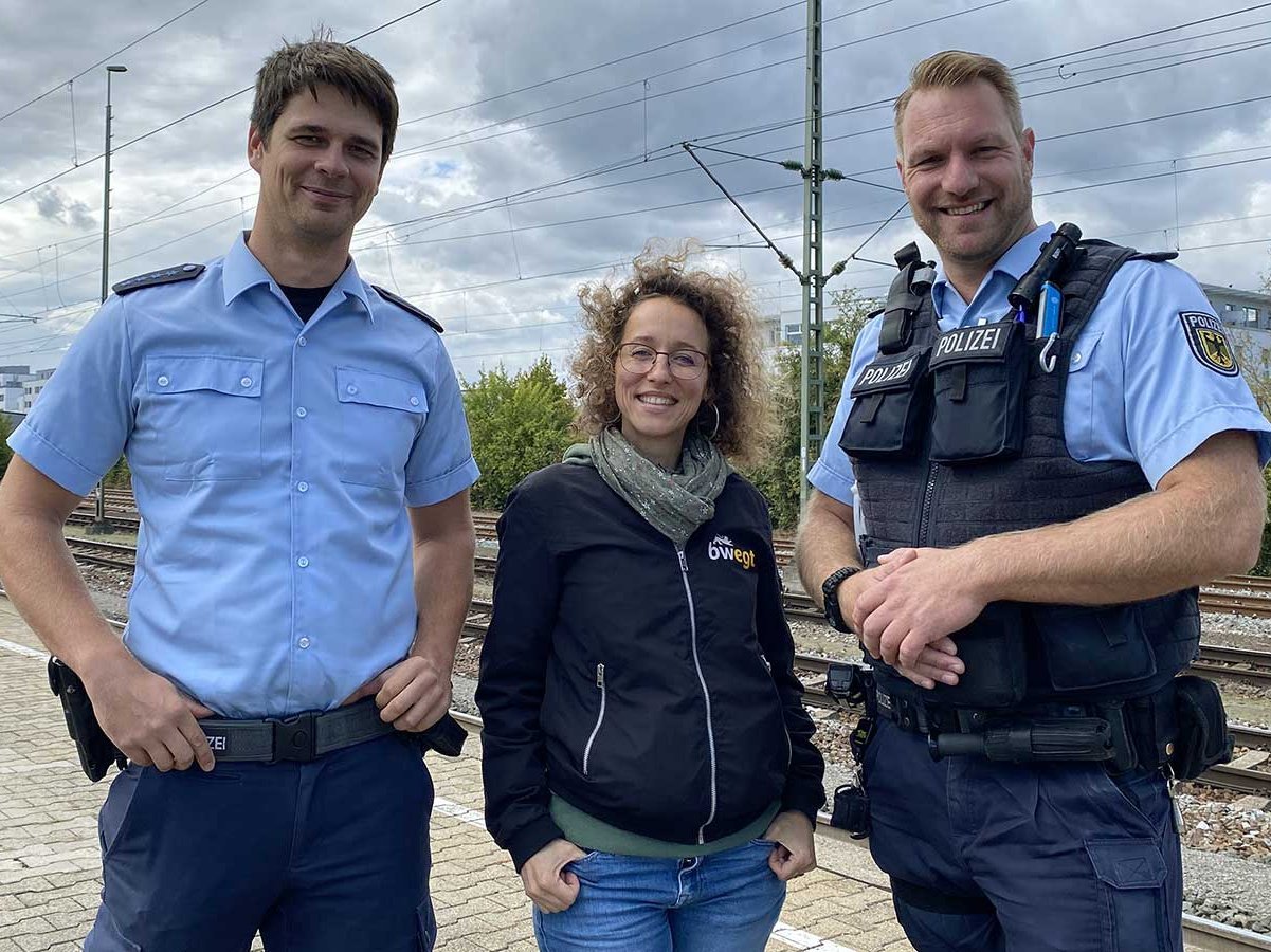 Frau steht zwischen zwei Polizisten am Bahngleis.