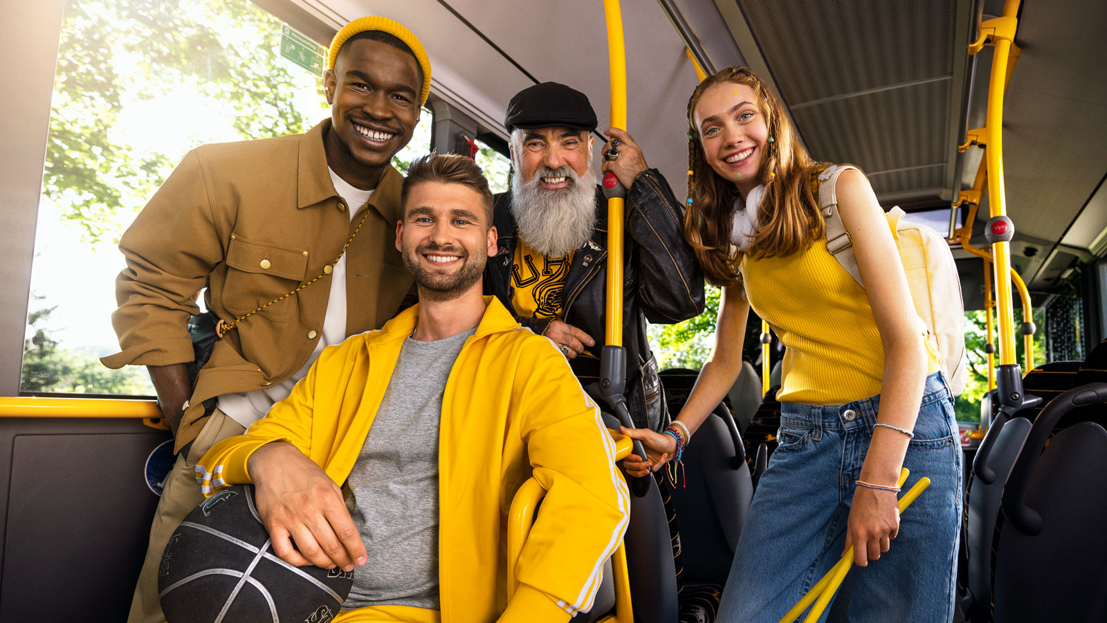 Eine Gruppe aus einem jungen Mann, einem älteren Mann, einem jungen Mann im Rollstuhl mit Basketball und einer Teenagerin mit Schlagzeugstöcken sitzt glücklich im Bus.