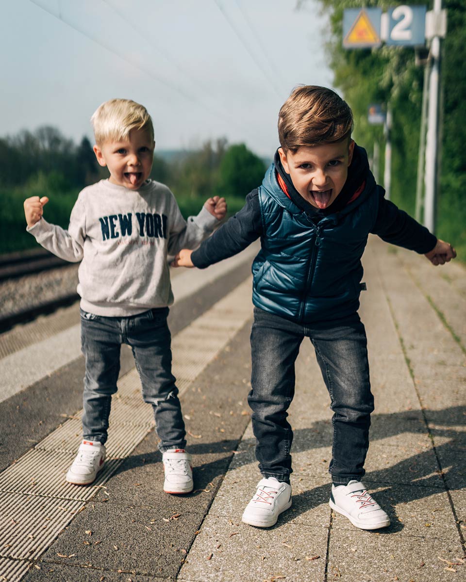 Zwei Jungen schneiden am Bahngleis Grimassen.