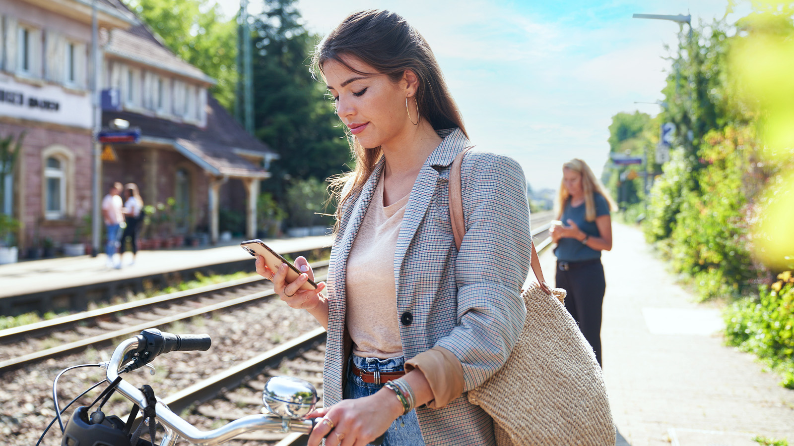 Junge Frau mit Smartphone in der Hand an einem Bahnhof