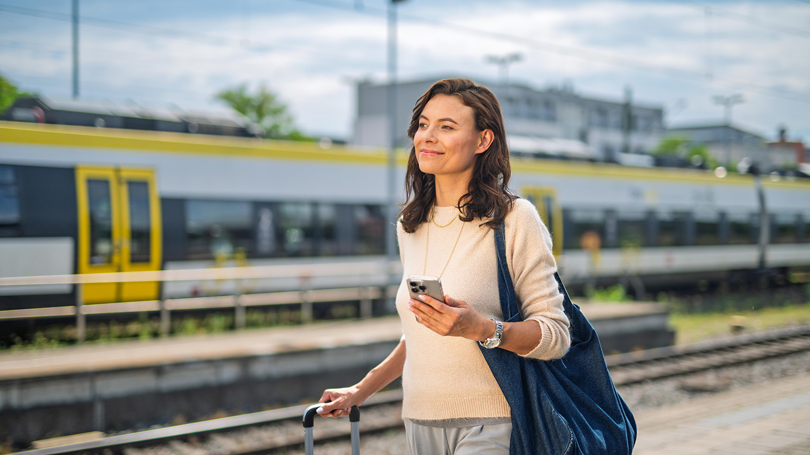 Eine Geschäftsfrau läuft mit ihrem Handy in der Hand am Bahnsteig entlang 