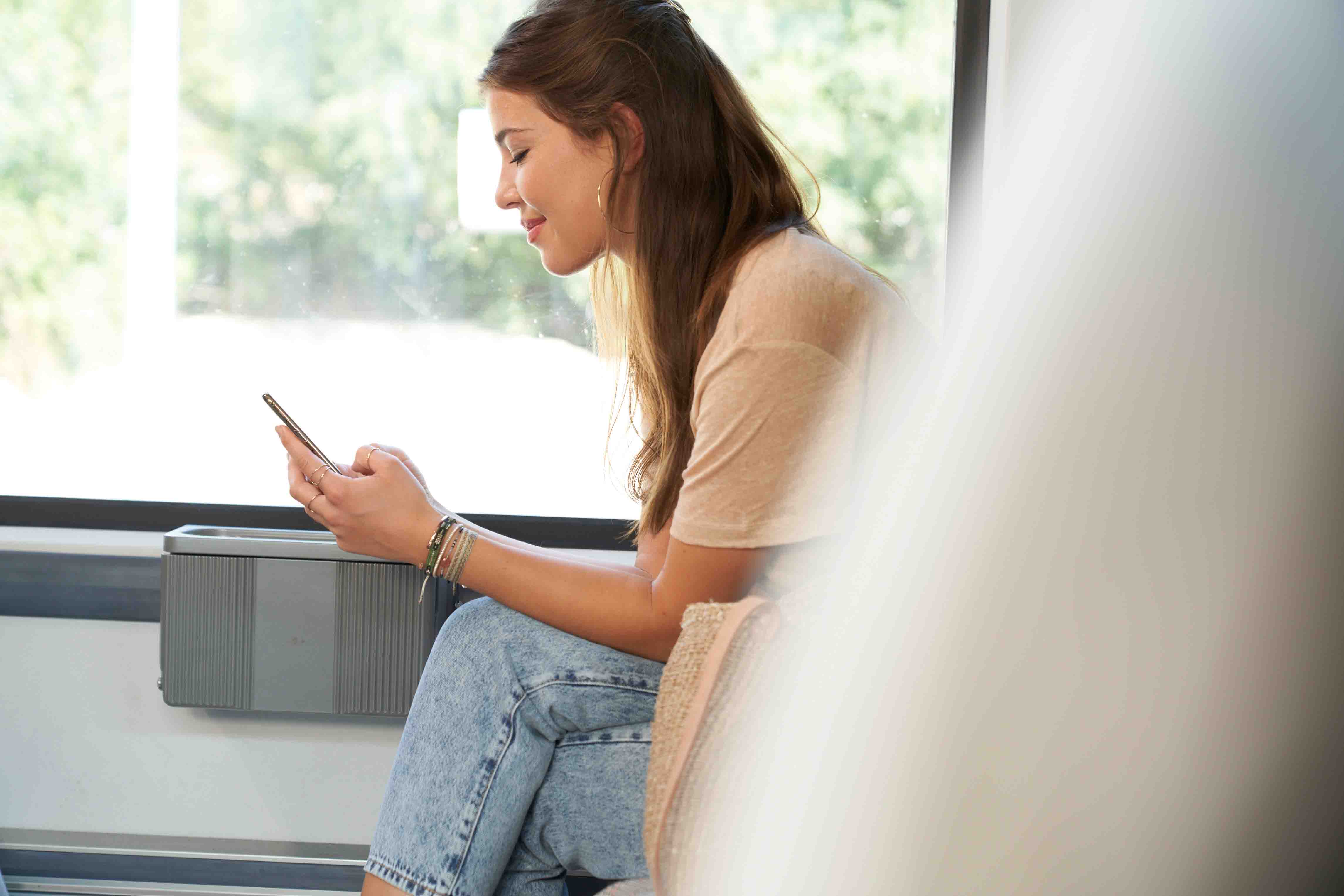 Junge Frau im Profil, die während einer Zugfahrt auf dem Smartphone tippt