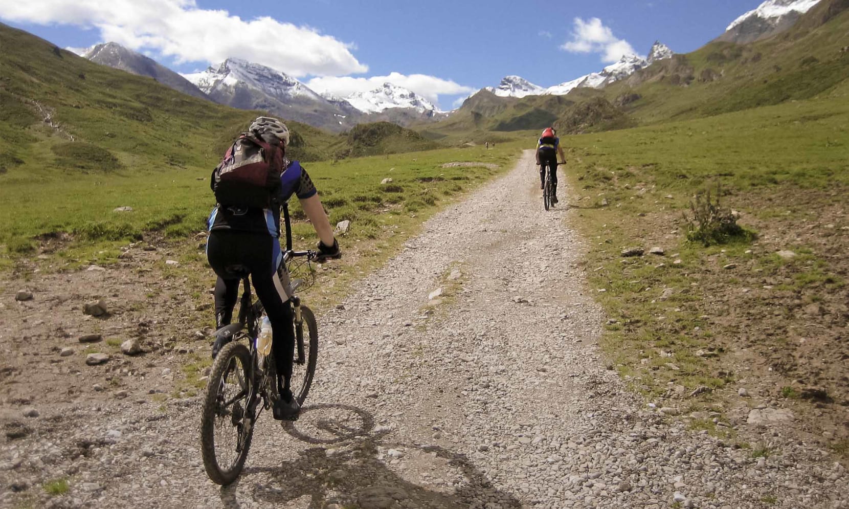 Ein Mountainbiker fährt auf einem bergigen Fahrradweg, in der Ferne sehen wir einen Fußgänger