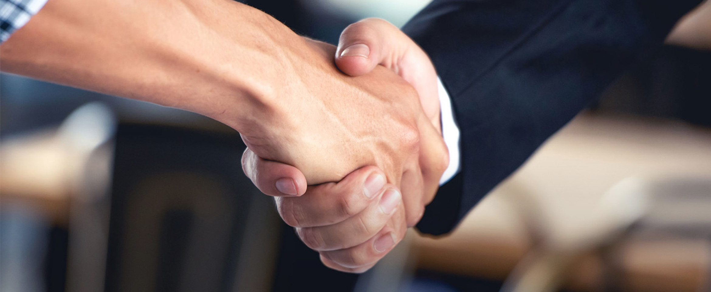 Nahaufnahme eines Handschlag von einem Mann im Business-Outfit und einem Mann im legeren Hemd