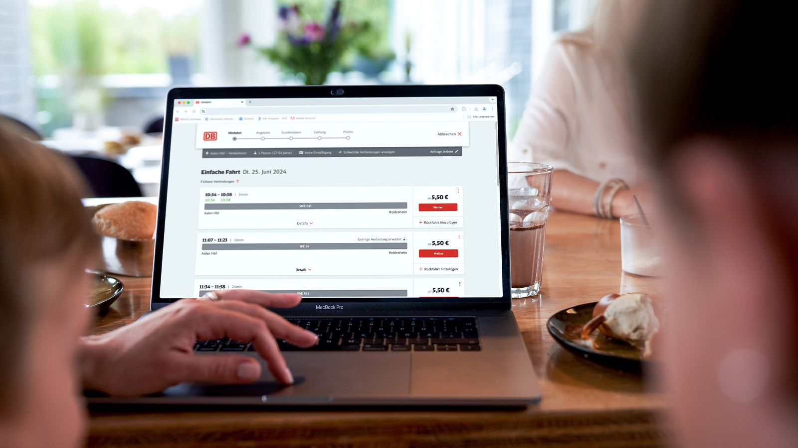 POV-Sicht auf einen Laptop mit der DB-Fahrplanauskunft und einer tippenden Hand auf dem Touch-Pad