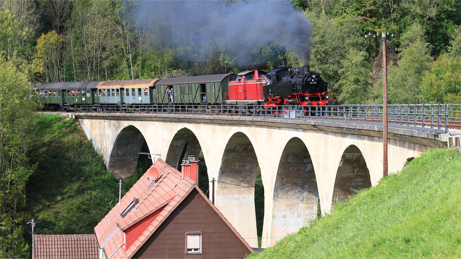 Eine rußende Dampflokomotive, die über eine Eisenbahnbrücke zum nächsten Dorf fährt