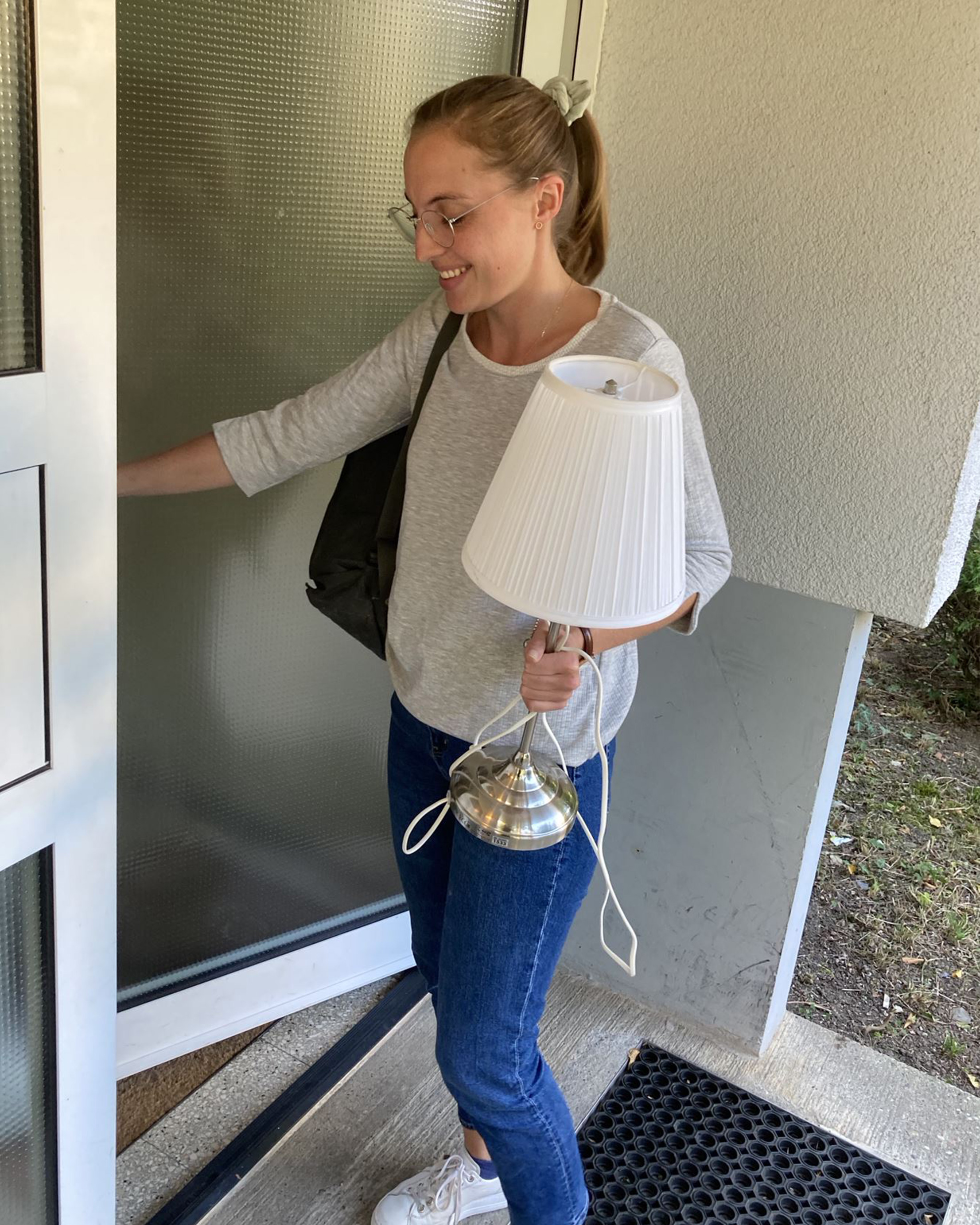 Junge Frau steht mit Lampe in der Hand vor einer Wohnungstür.