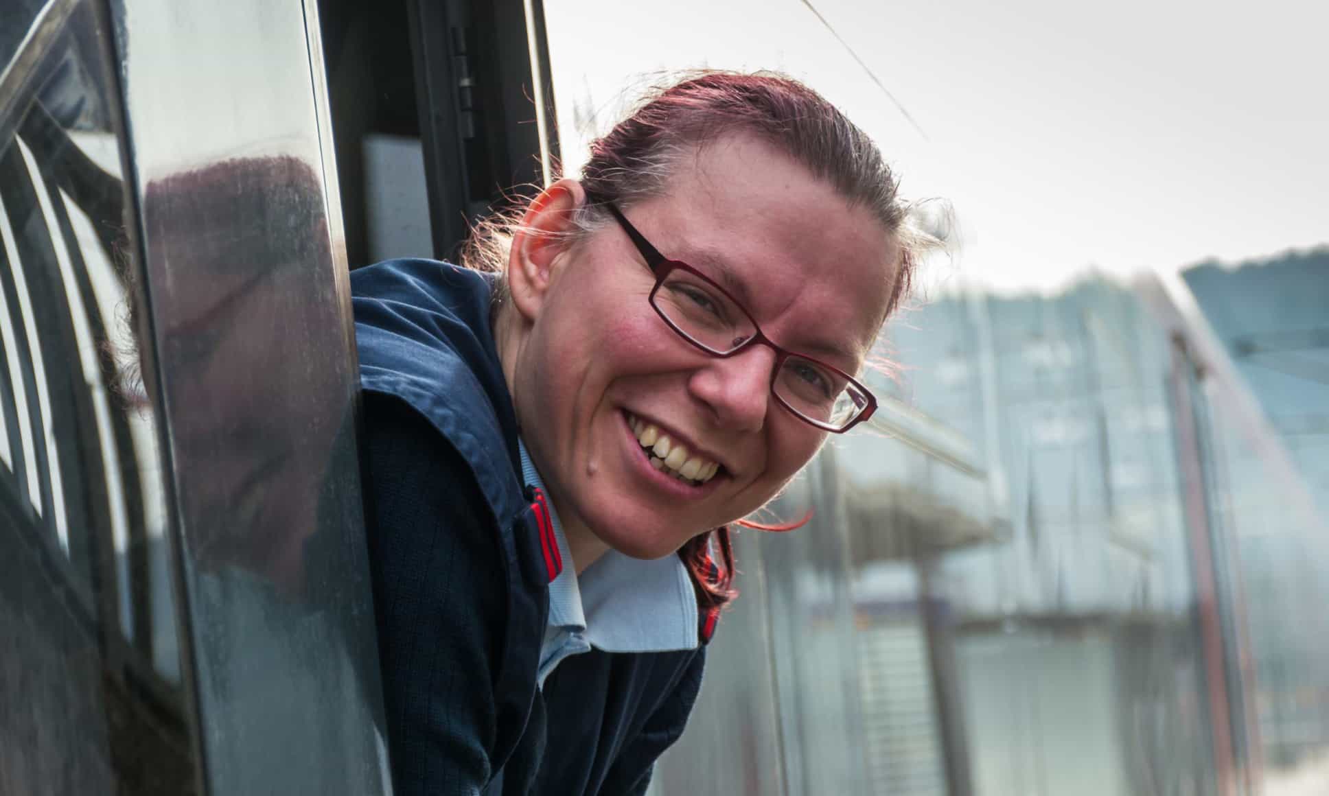 Lokführerin mit Brille lehnt sich und schaut seitlich aus Zugfenster.