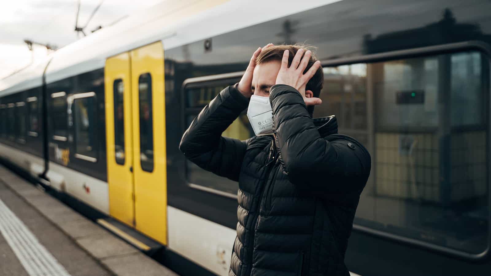 Mann steht an Bahngleis und schlägt sich verärgert die Hände vor das Gesicht.