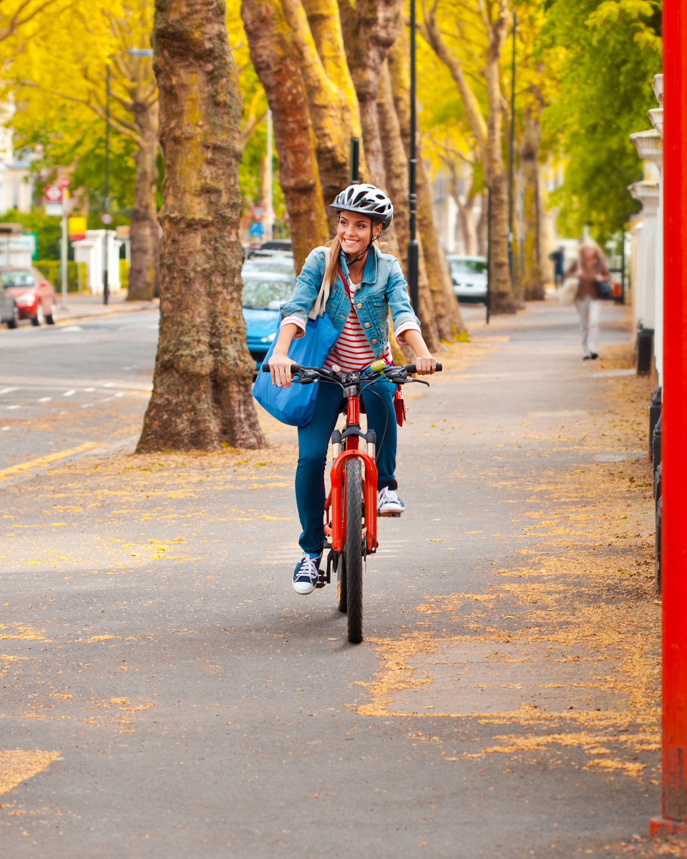 Frau fährt lächelnd auf ihrem Fahrrad über einen Weg, der mit Bäumen gesäumt ist.