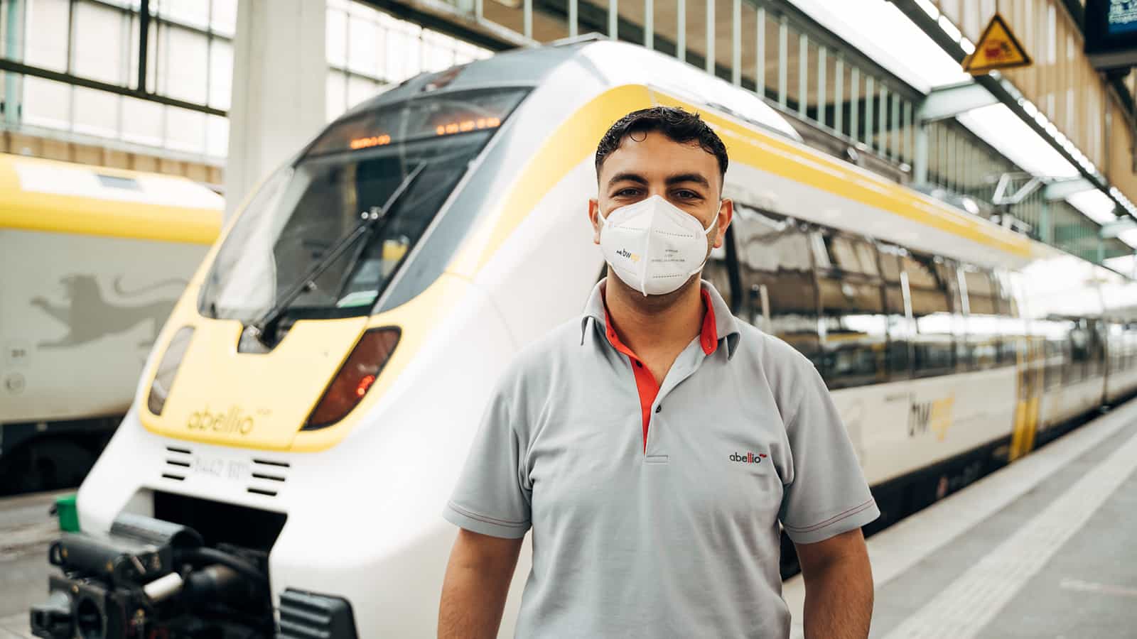 Mann mit Maske steht am Bahngleis vor einem Zug von bwegt.