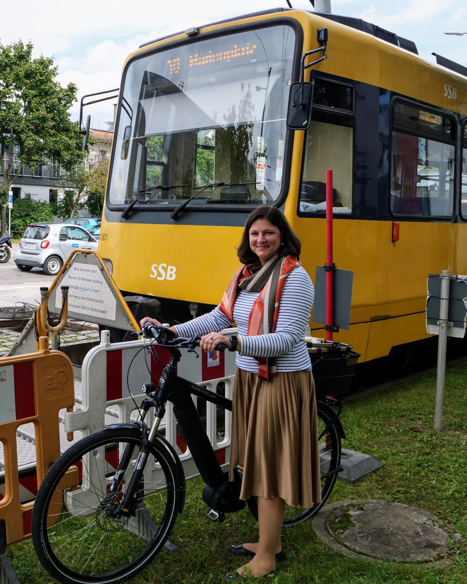 Frau mit Fahrrad steht neben Straßenbahn.