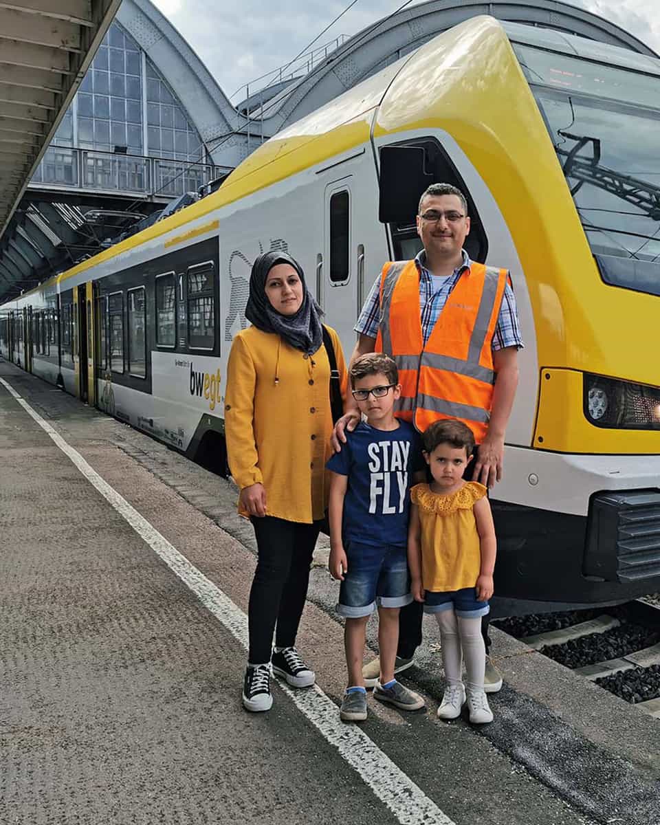 Lokführer steht mit seiner Familie vor einer Bahn am Bahnsteig.