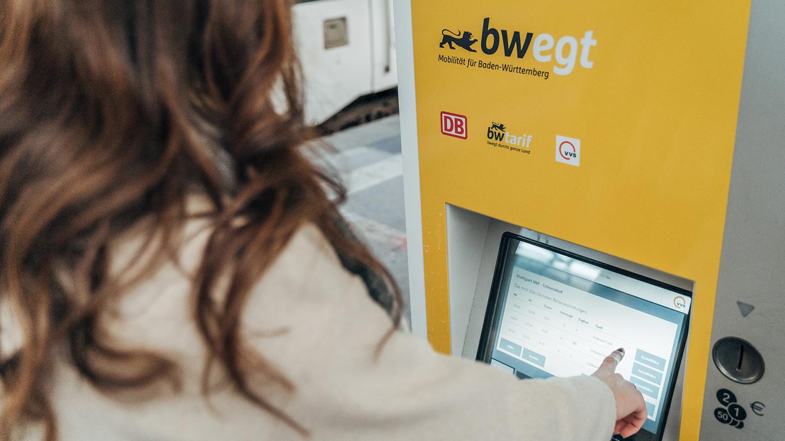 Blick über die Schulter einer Frau, die gerade am Ticketautomat etwas antippt.