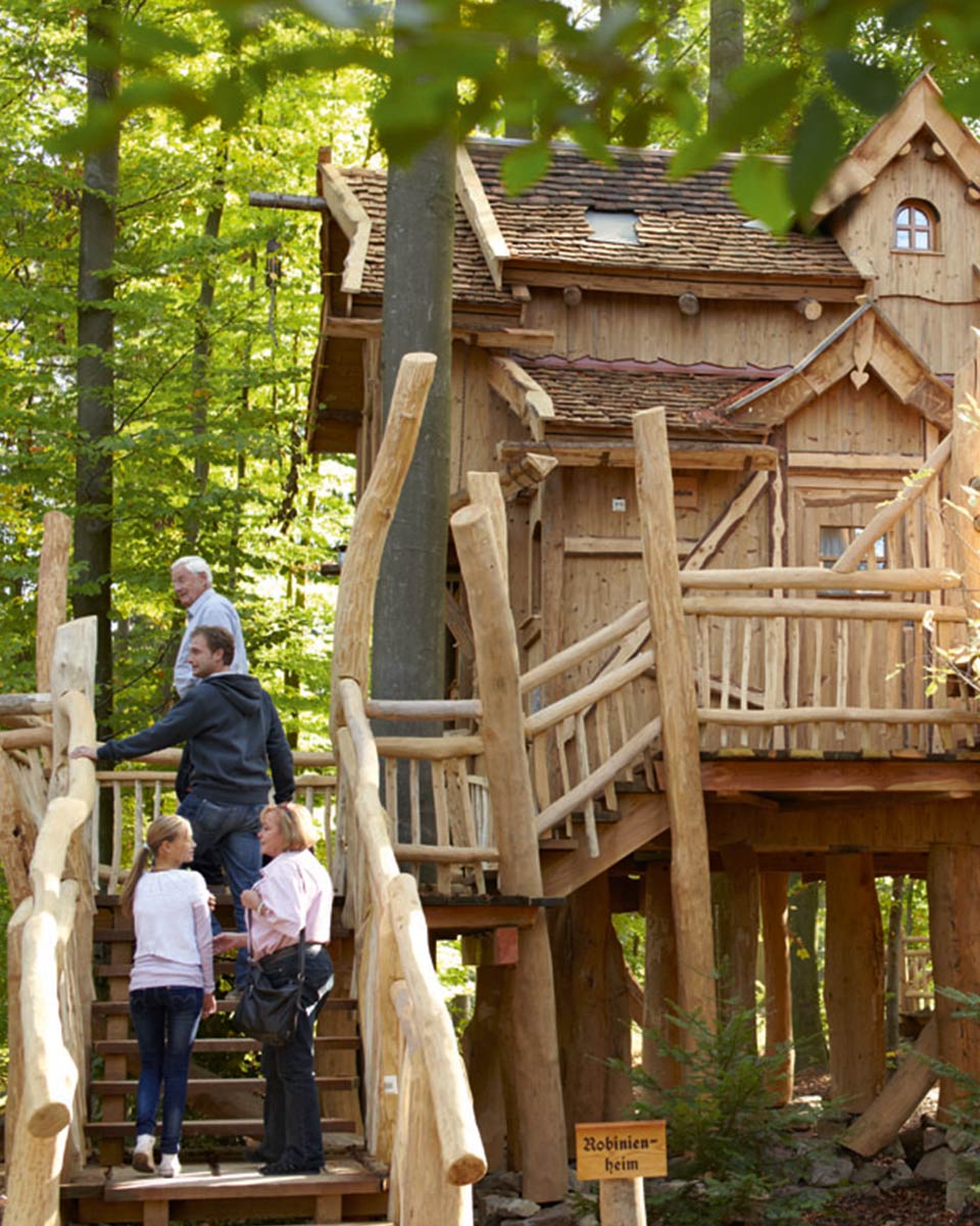 Mehrere Personen gehen die Treppe zu einem großen Baumhaus hoch.