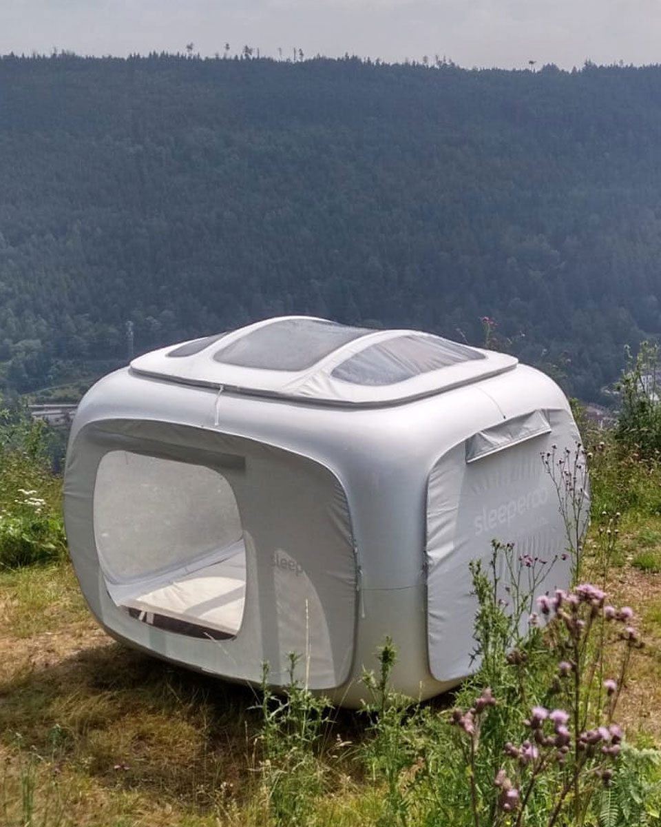 Ein weißes, futuristisch anmutendes Zelt steht mitten in der Natur mit Blick über den Wald.