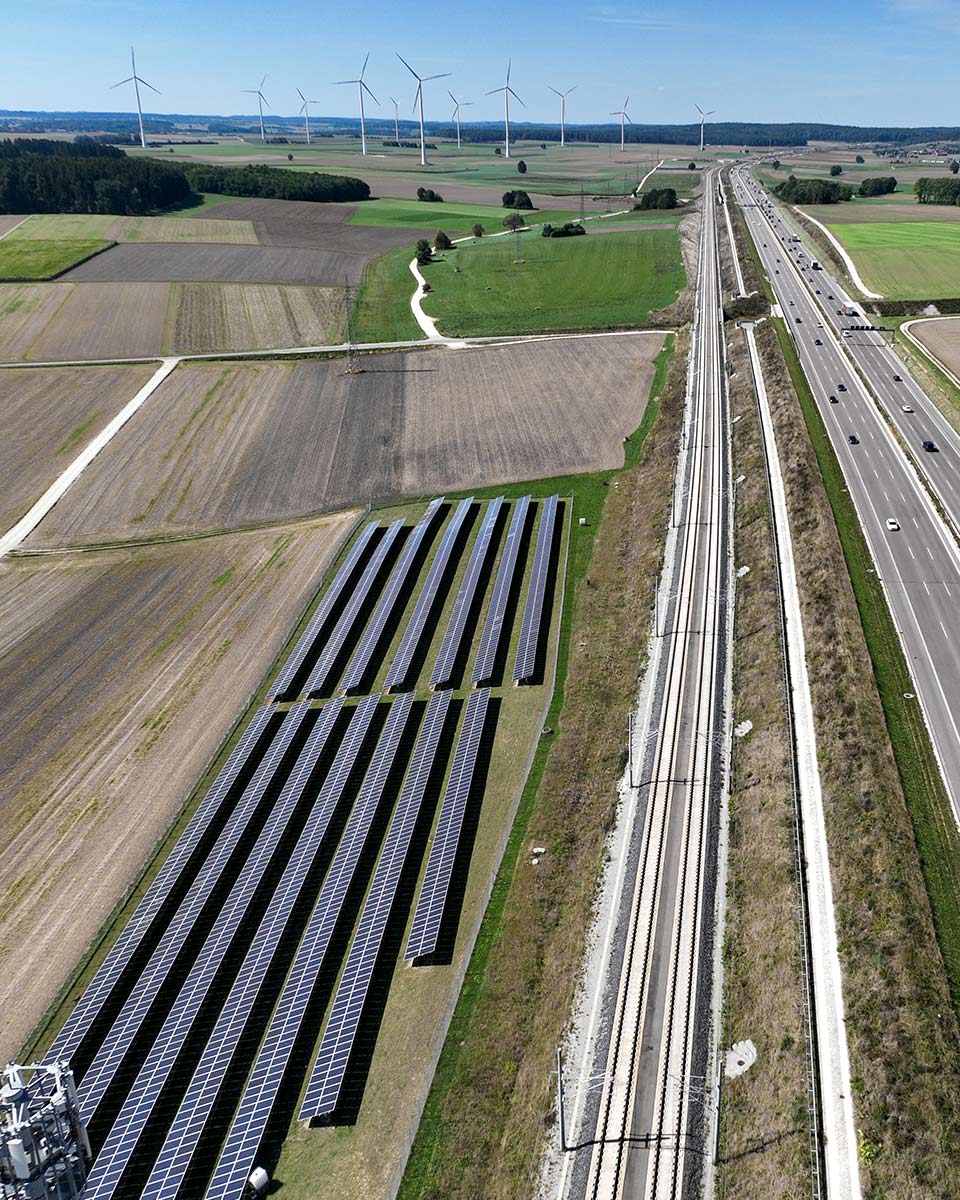 Blick von der Vogelperspektive auf eine Bahnstrecke neben Autobahn und Feld.