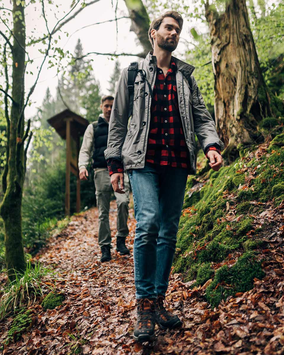 Zwei junge Männer gehen einen leicht abschüssigen Pfad im Wald herunter.