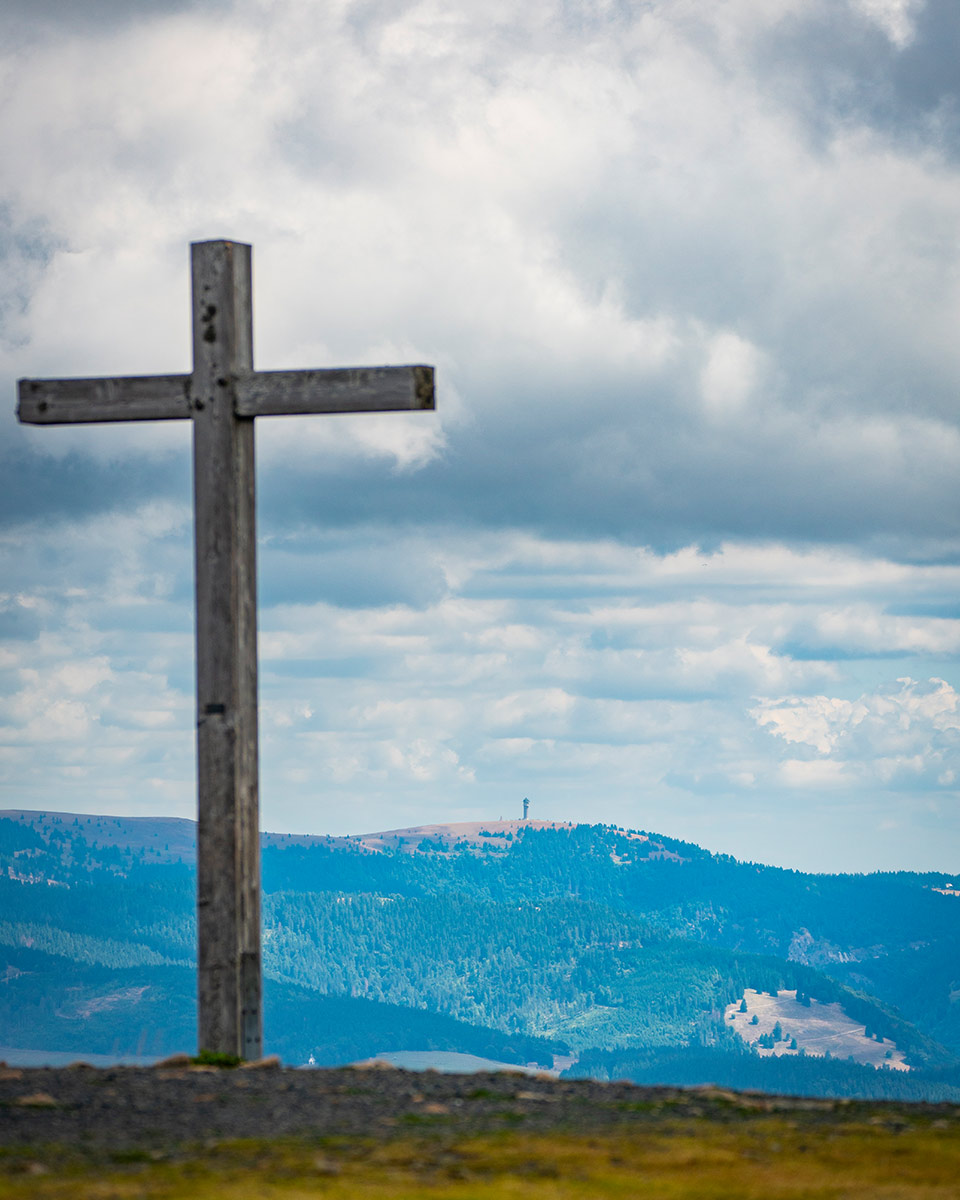 Auf einer Anhöhe steht ein Kreuz aus Holz.