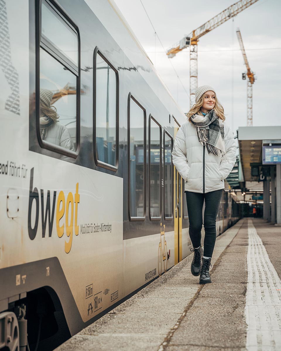 Junge Frau läuft am Bahnsteig neben einer Bahn entlang.