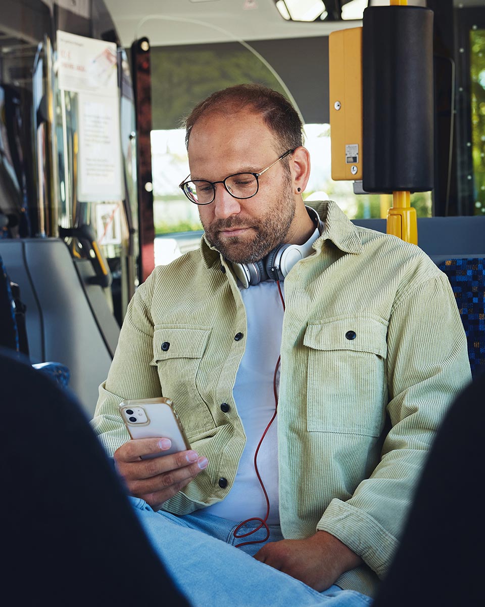 Mann sitzt mit Smartphone in der Hand im Bus.