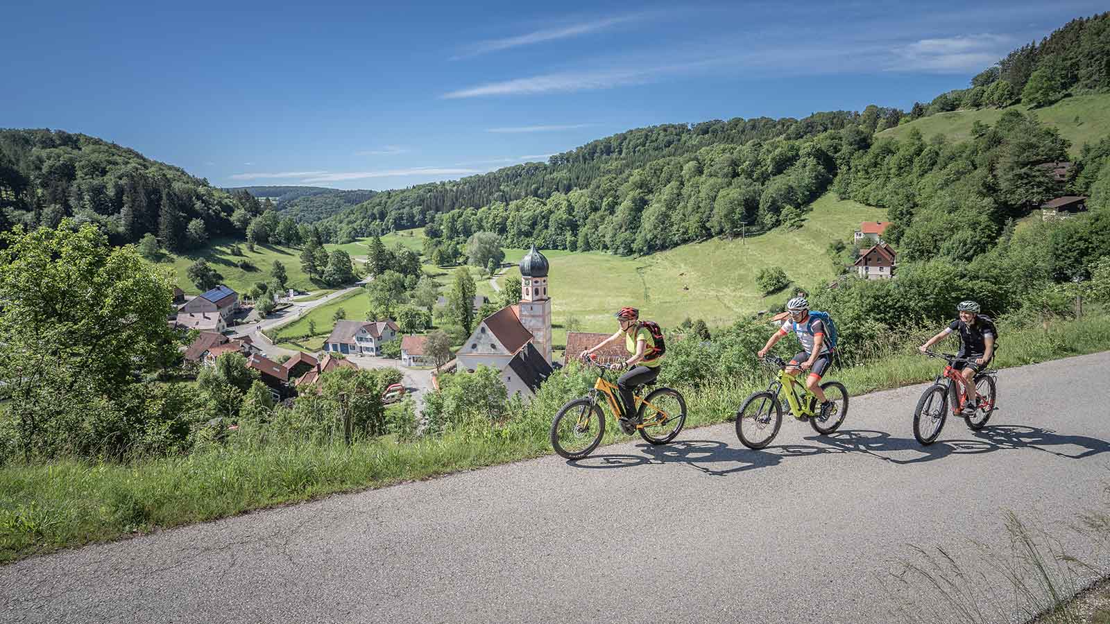 Drei Fahrradfahrer fahren auf einer Straße durch die Natur.