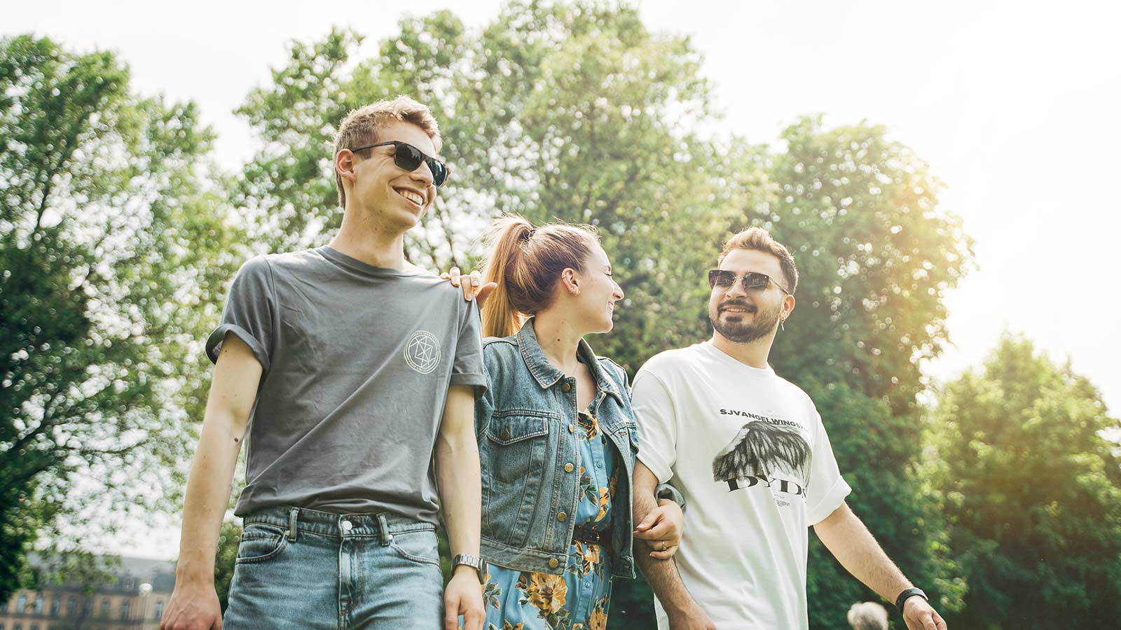 Drei junge Leute laufen bei Sonnenschein durch den Park.