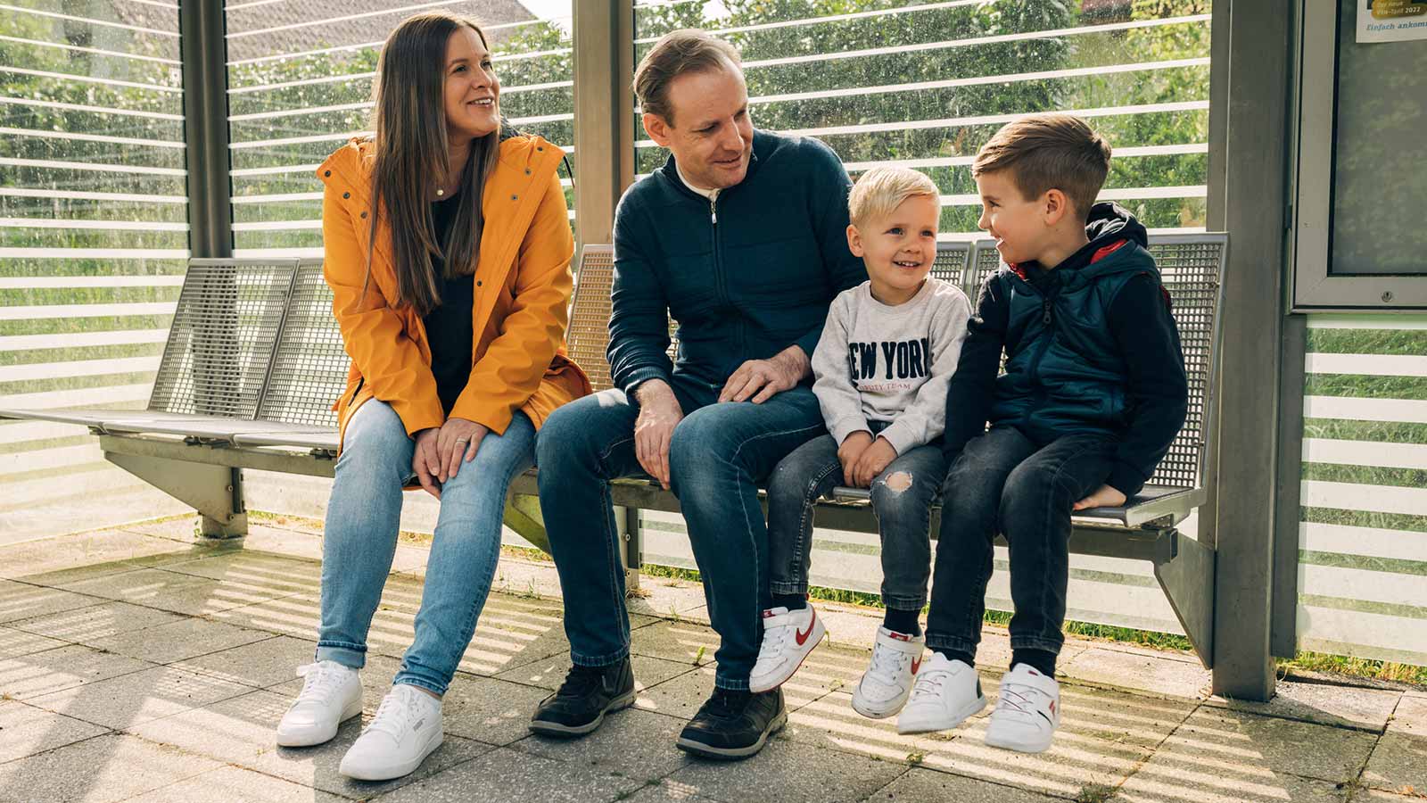 Familie mit zwei Kindern sitzt an einer Bahnhaltestelle.