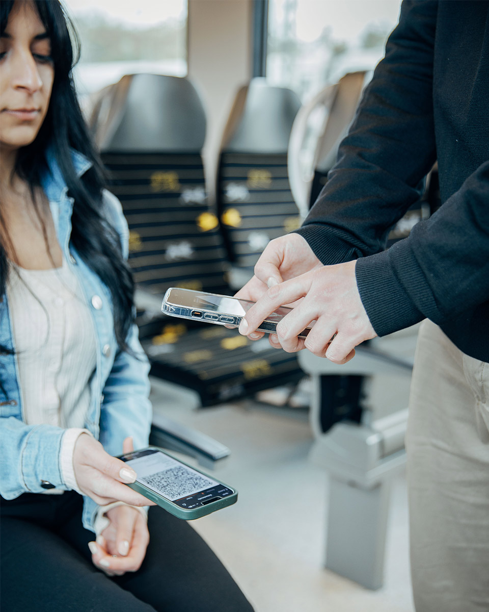 Fahrkartenkontrolle bei einer jungen Frau, die ihre Fahrkarte auf dem Smartphone vorzeigt.