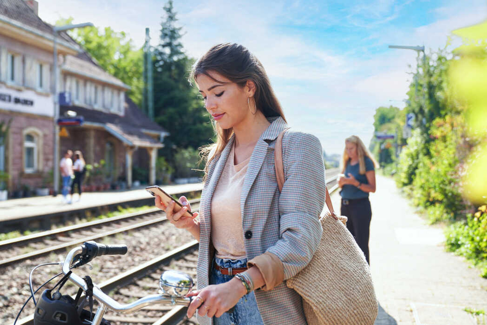 Junge Frau mit Smartphone in der Hand an einem Bahnhof